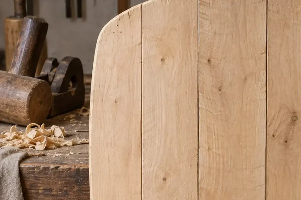 Detail of an explanatory workshop reconstruction: a wooden mallet, a plane and wood shavings on a bench beside the edge of an unfinished plank shield core.