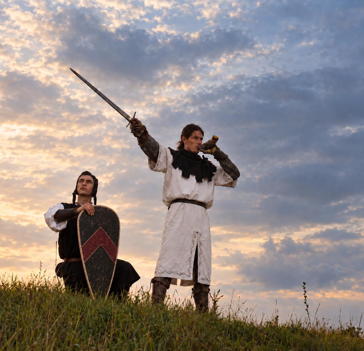 Two reenactors at dusk, one raising a sword, the other holding a heater shield